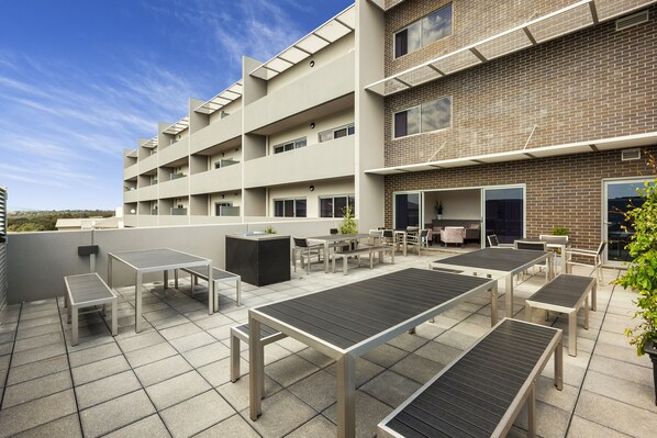 A rooftop terrace with outdoor seating and a brick building in the background. - Quest Bundoora (Bundoora)