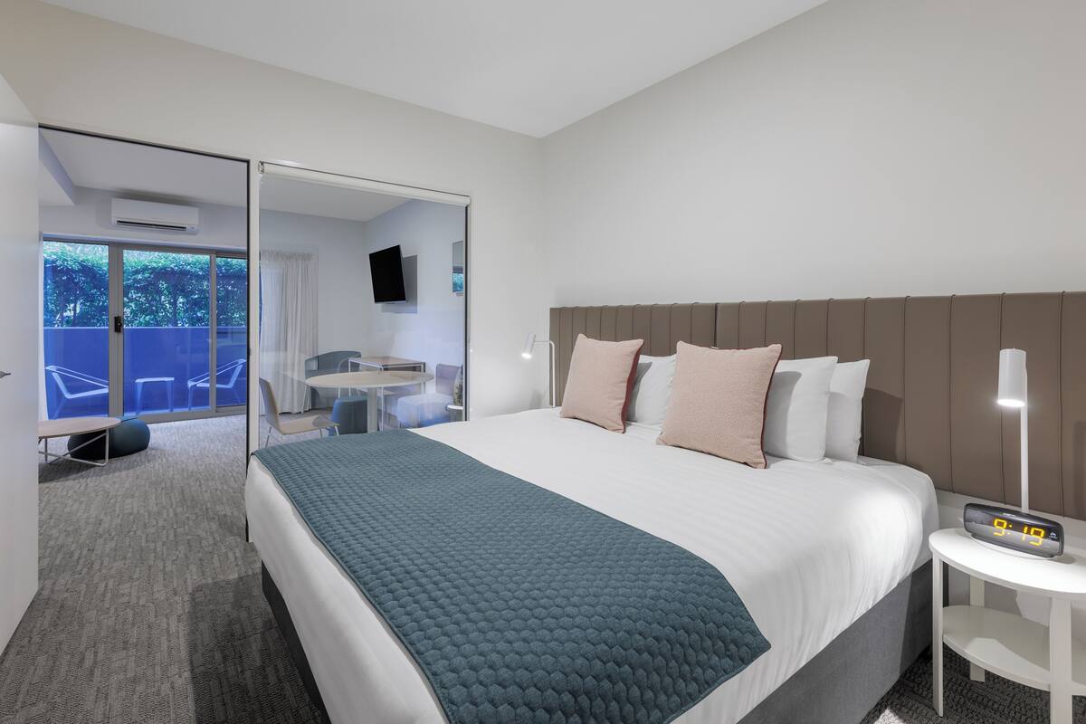 Ein modernes Hotelzimmer mit einem großen Bett, einem Nachttisch, einem Schreibtisch und einem Stuhl.
