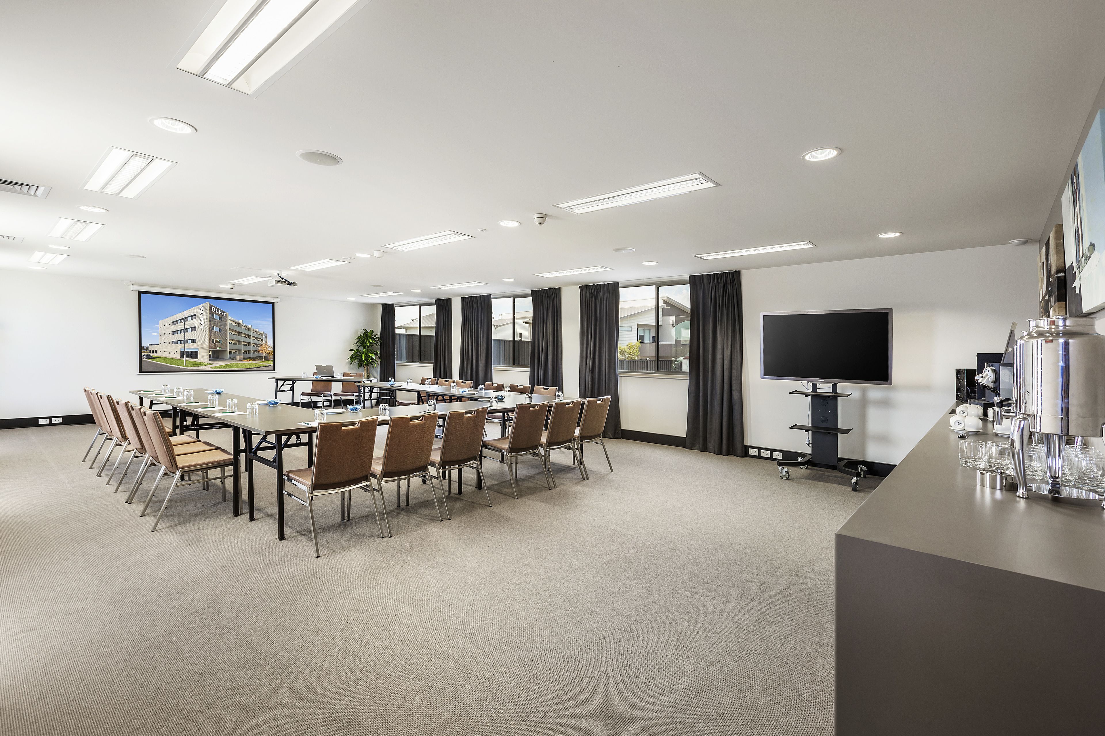 A conference room with a long table, chairs, a projector screen, and a TV.