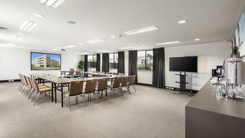 A conference room with a long table, chairs, a projector screen, and a TV.