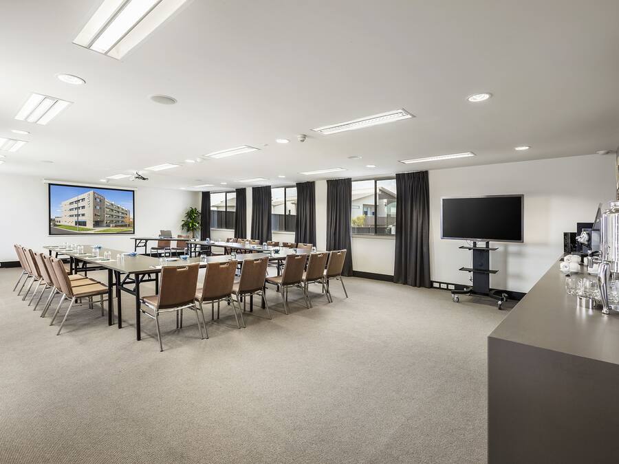 A conference room with a long table, chairs, a projector screen, and a TV.
