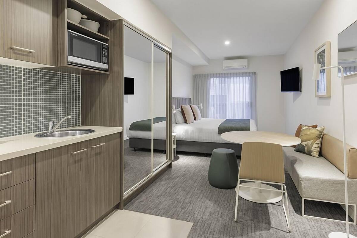 Ein modernes Hotelzimmer mit Küchenzeile, einem Bett, einer Couch und einem Essbereich.