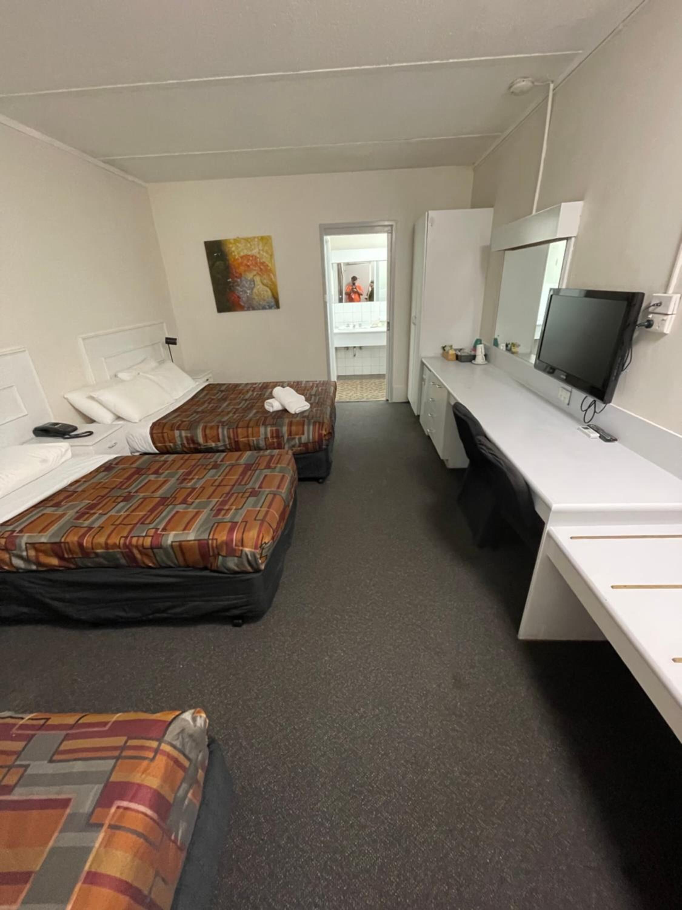 Une chambre d’hôtel avec deux lits, un bureau, une télévision et une salle de bain visible à travers une porte ouverte.