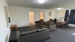 A spacious living area with a large sectional sofa, a dining table with chairs, and a small side table. - Parkside Inn Motel (Kingsbury)