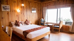 A wooden-paneled room with a large bed, a chair, a small table, and a window with curtains. - Himalayan Deurali Resort (Pokhara)