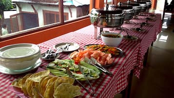 A buffet table with various dishes and utensils, set against a window with a view of a house.