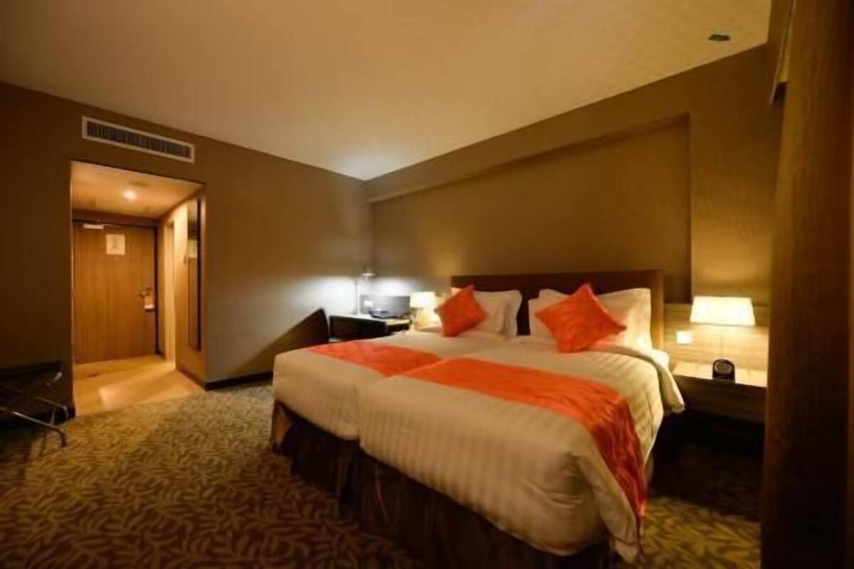 A hotel room with a large bed, two bedside tables, a nightstand, and a carpeted floor.