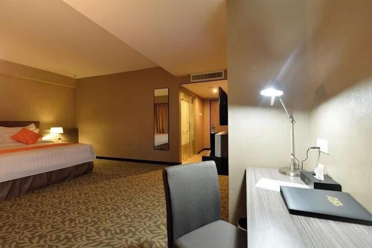 A hotel room with a bed, a desk, a chair, a lamp, and a mirror.