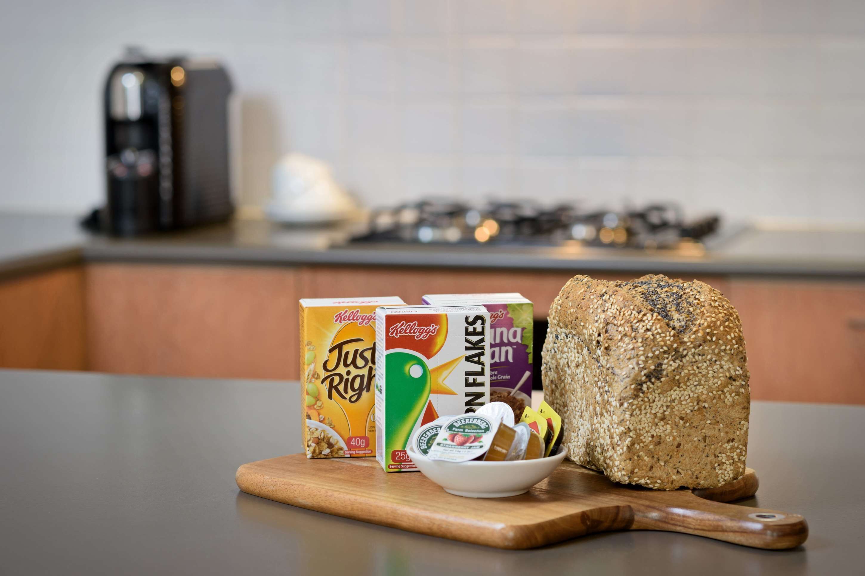 Un piano di lavoro in cucina con una pagnotta di pane, due scatole di cereali Kellogg's e una ciotola di yogurt.