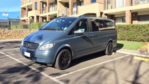 Una camioneta gris estacionada en un estacionamiento, con un edificio de apartamentos de ladrillo al fondo.