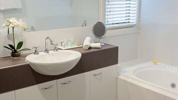 A bathroom with a white sink, a mirror, a bathtub, and a window with blinds.