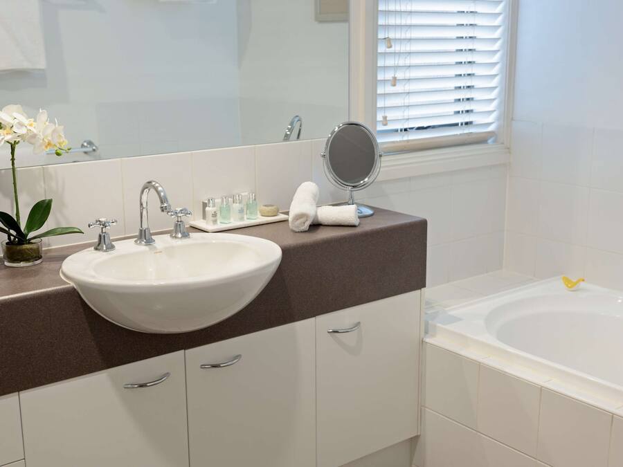 A bathroom with a white sink, a mirror, a bathtub, and a window with blinds.