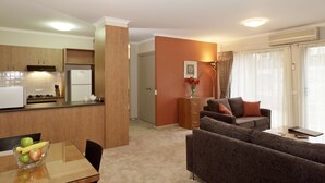 Un espacio habitable compacto con kitchenette, una zona de comedor y una sala de estar con sofá y mesa de centro.