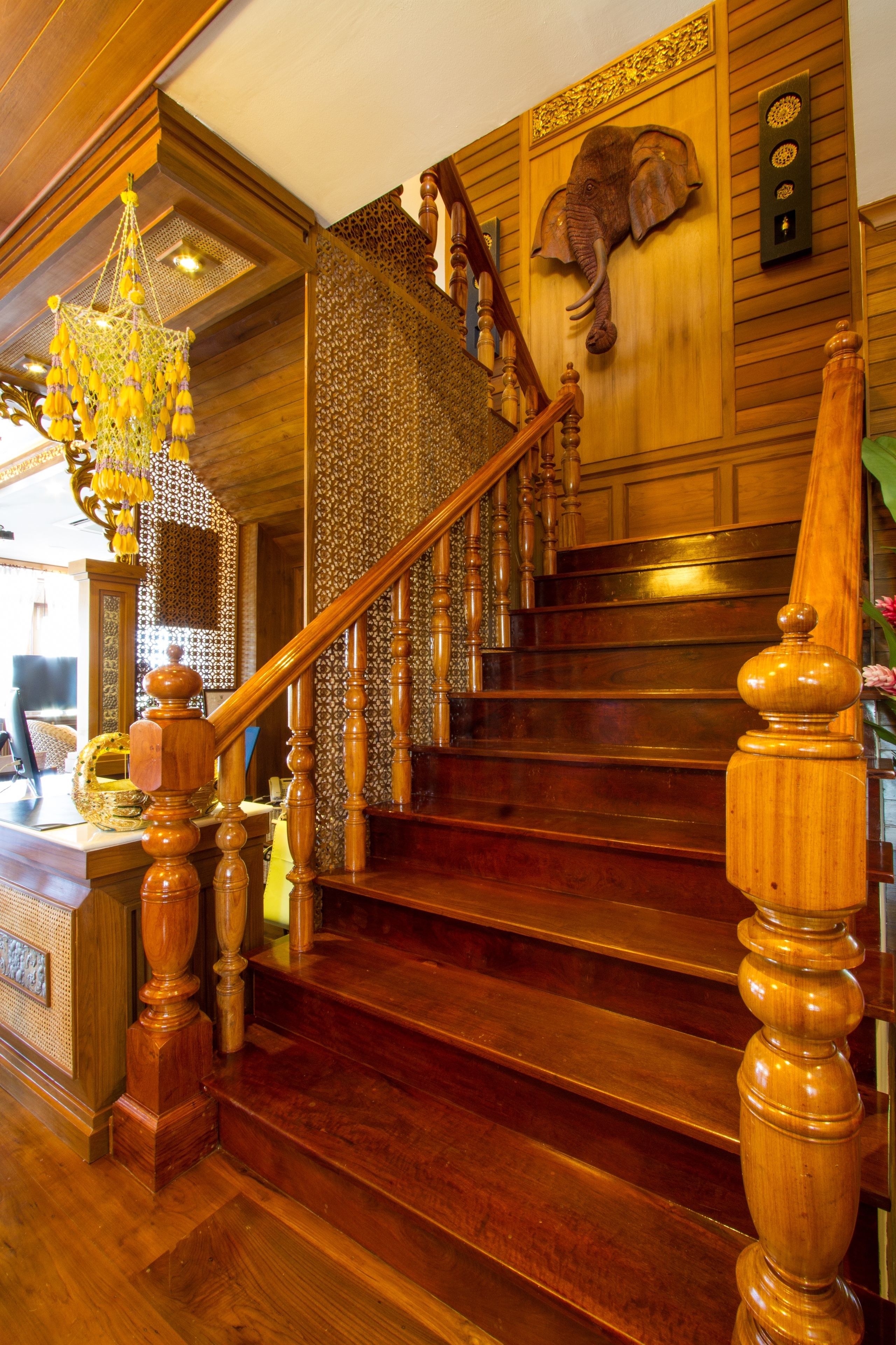 A wooden staircase with a decorative elephant head, a chandelier, and a patterned wall.