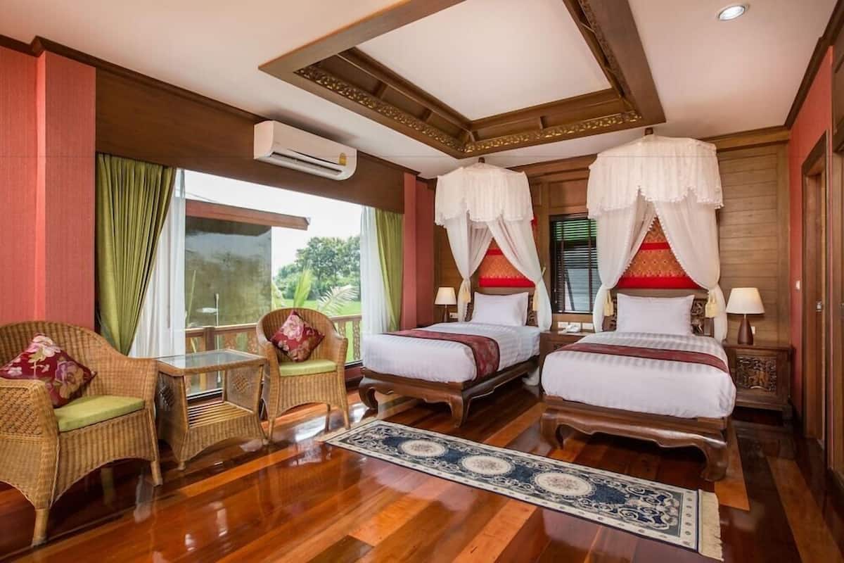 Una habitación de hotel con dos camas, un área de descanso con una silla y una mesa, y un ventanal grande.