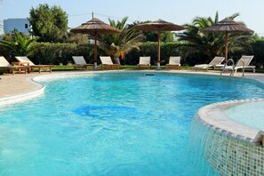 Una piscina al aire libre, sombrillas, sillones reclinables de piscina