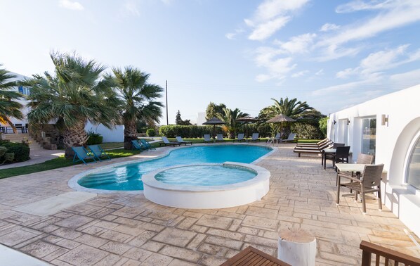 Una piscina al aire libre, sombrillas, sillones reclinables de piscina