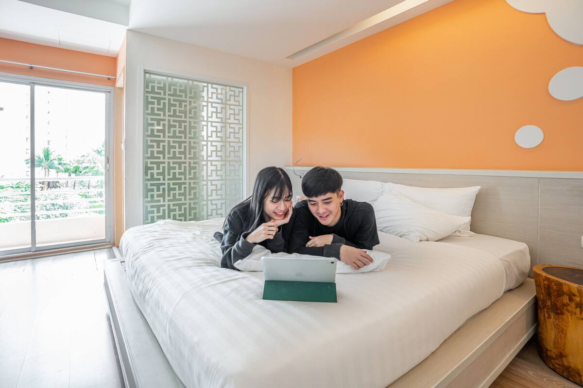 Un dormitorio moderno con una cama grande, una computadora portátil sobre la cama y vistas al exterior a través de una puerta corrediza.