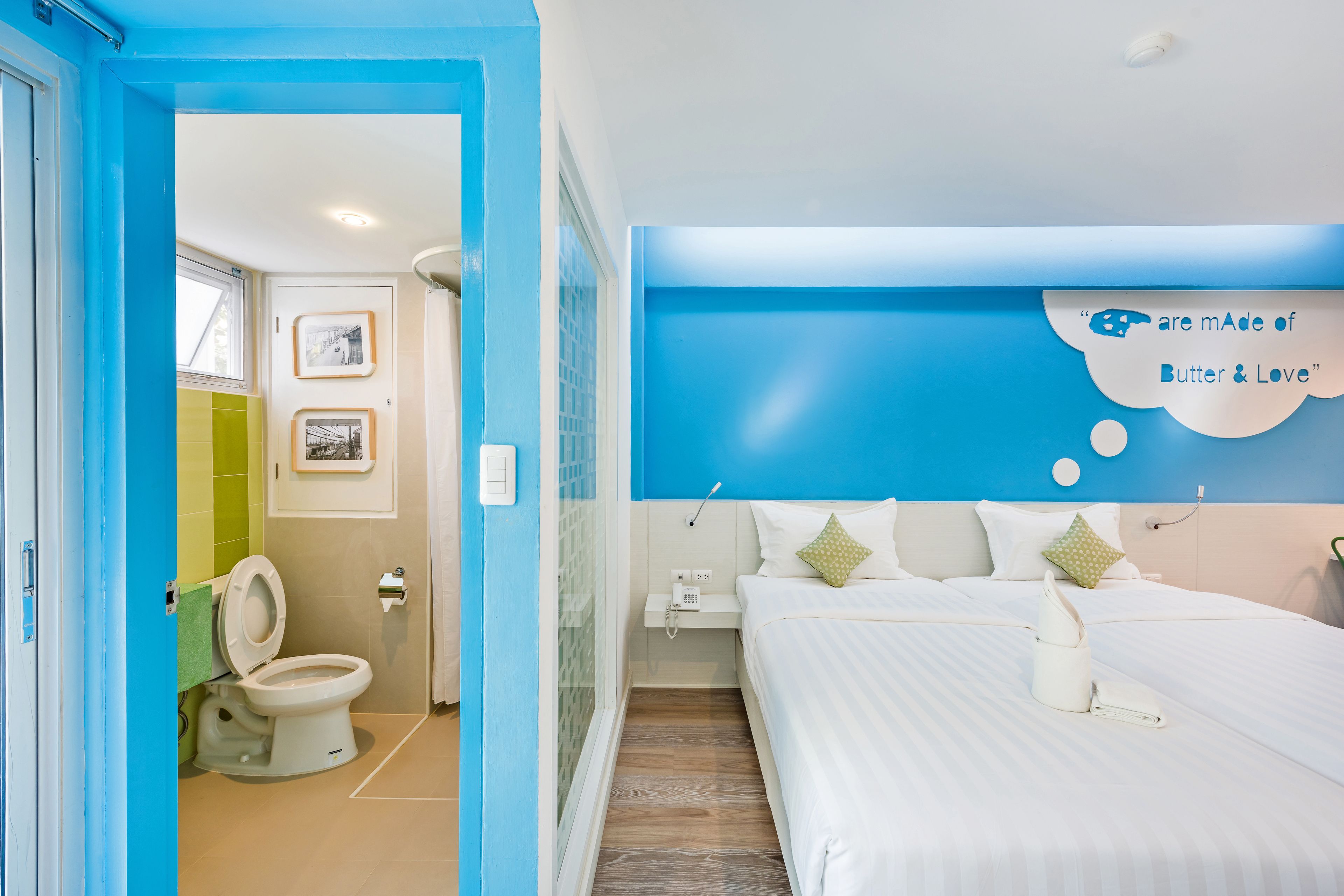 A hotel room with a blue accent wall, a bed with white bedding, a bedside table with a phone, and a wall-mounted artwork.