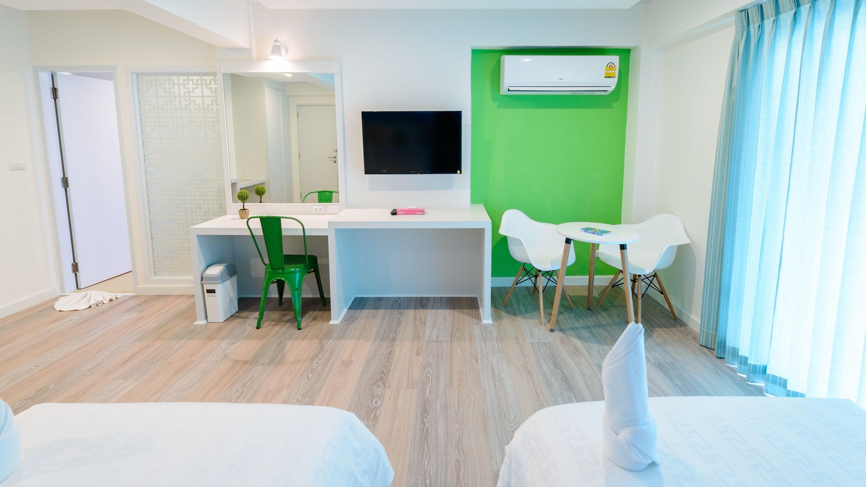 A hotel room with a desk, two chairs, a TV, an air conditioner, and a bed.