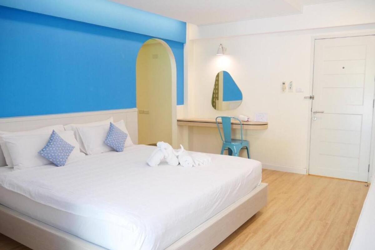 Una habitación de hotel con una cama grande, un escritorio con silla, un espejo y una puerta.