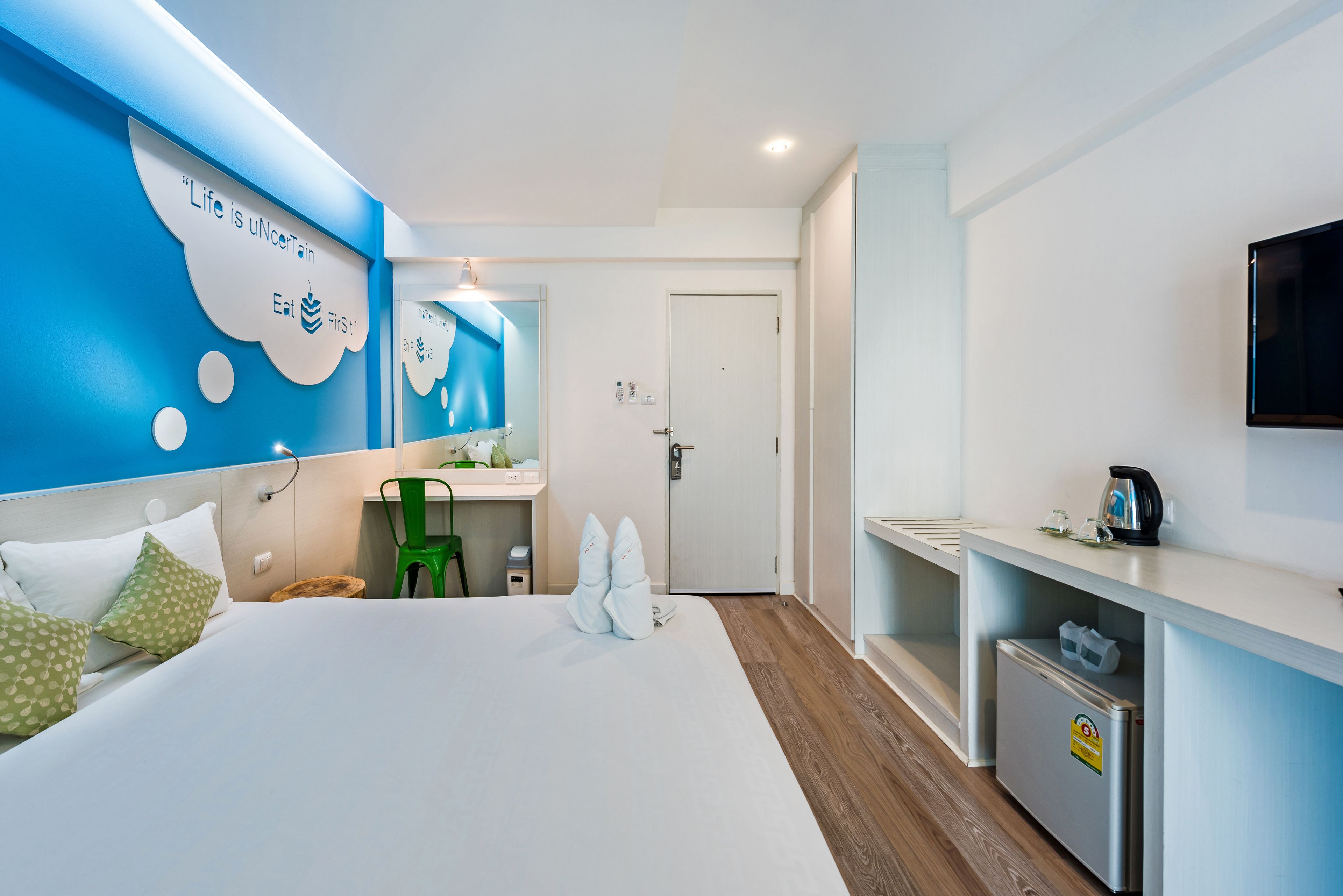 Ein modernes Hotelzimmer mit einem großen Bett, einem Schreibtisch, einem Spiegel, einem Fernseher und einer Minibar.