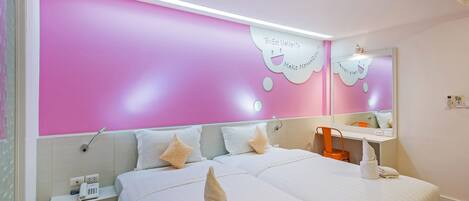 A hotel room with a pink accent wall, a bed with white bedding, a bedside table with a phone, and a mirror above the bed.