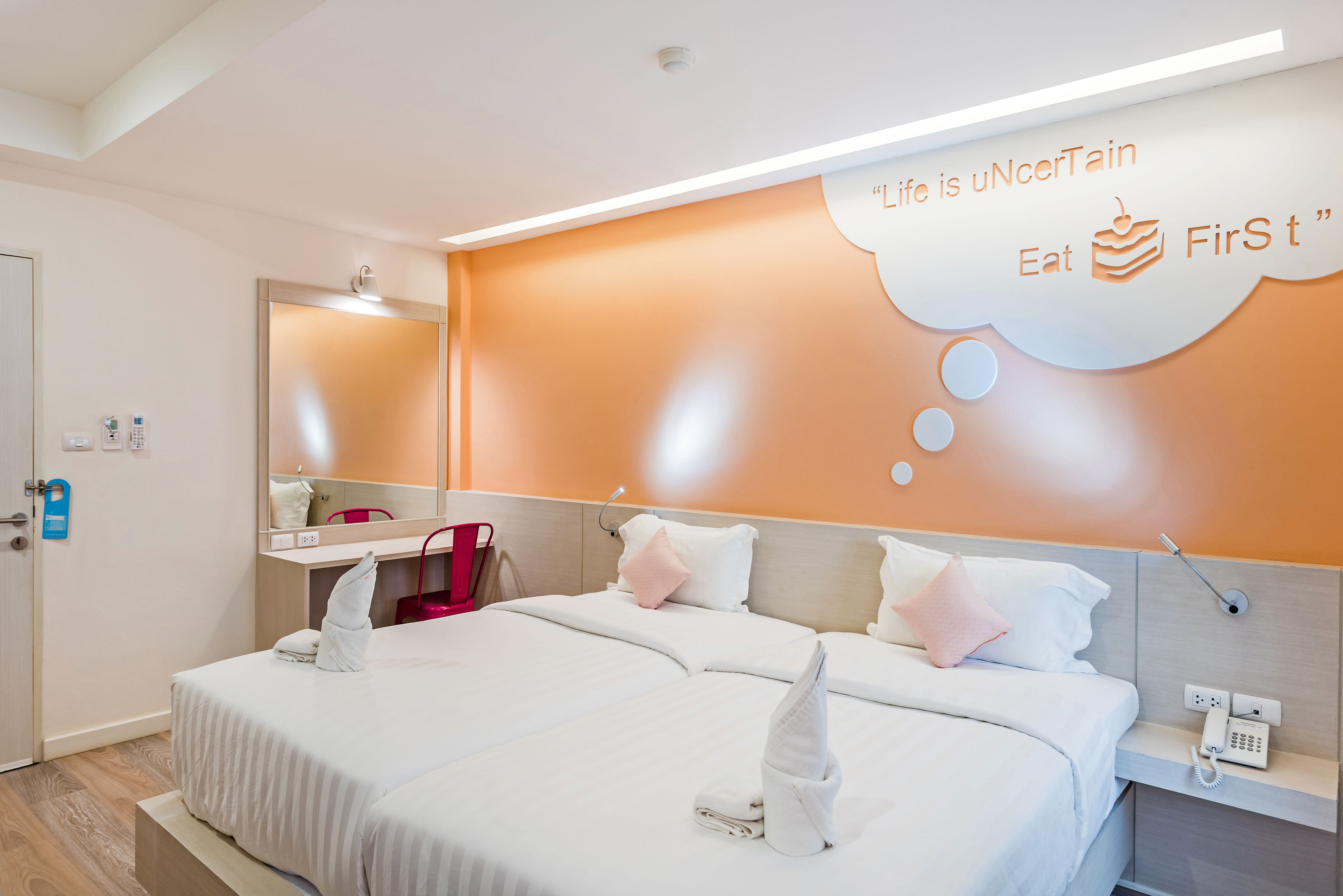 Habitación de hotel con dos camas, un espejo, un teléfono y una pared con una cita motivacional.