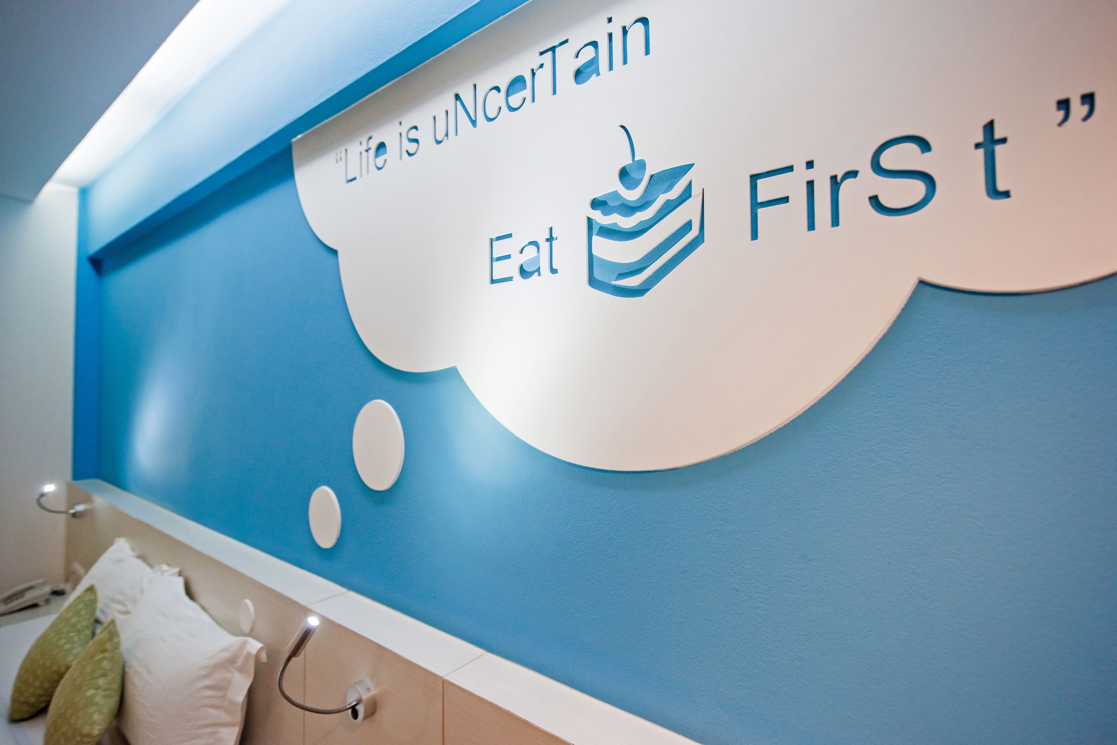 Una pared con un diseño azul y blanco, que incluye el texto 'Life is uncertain Eat First' e una ilustración de un pastel.