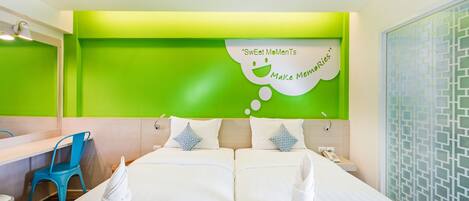 Et hotelværelse med to senge, en blå stol, et spejl og en væg med grønne detaljer samt en taleboble med teksten "Sweet MoMenTs Make Memories".