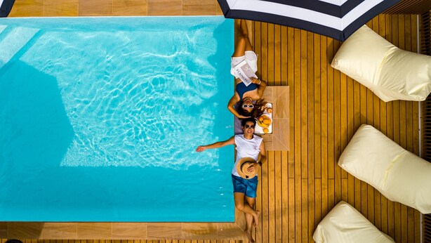 Vista aérea de una piscina con suelo de madera y sillas de lounge blancas.