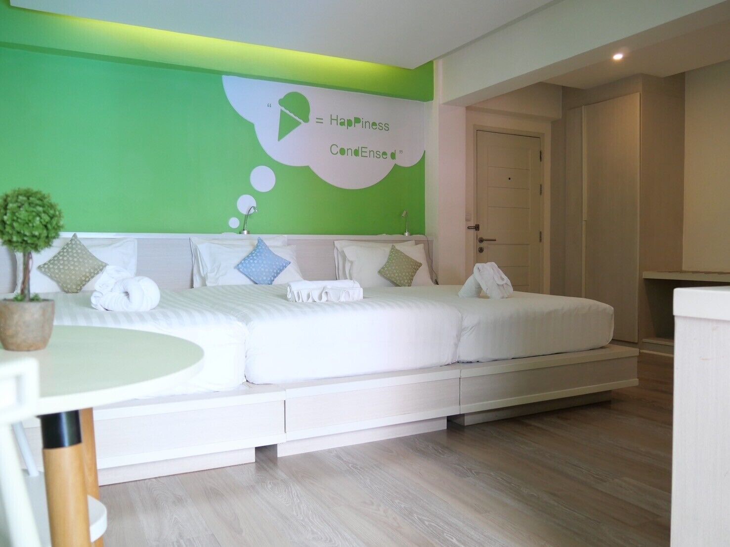 A modern bedroom with a green accent wall, a bed with white bedding, and a small potted plant.
