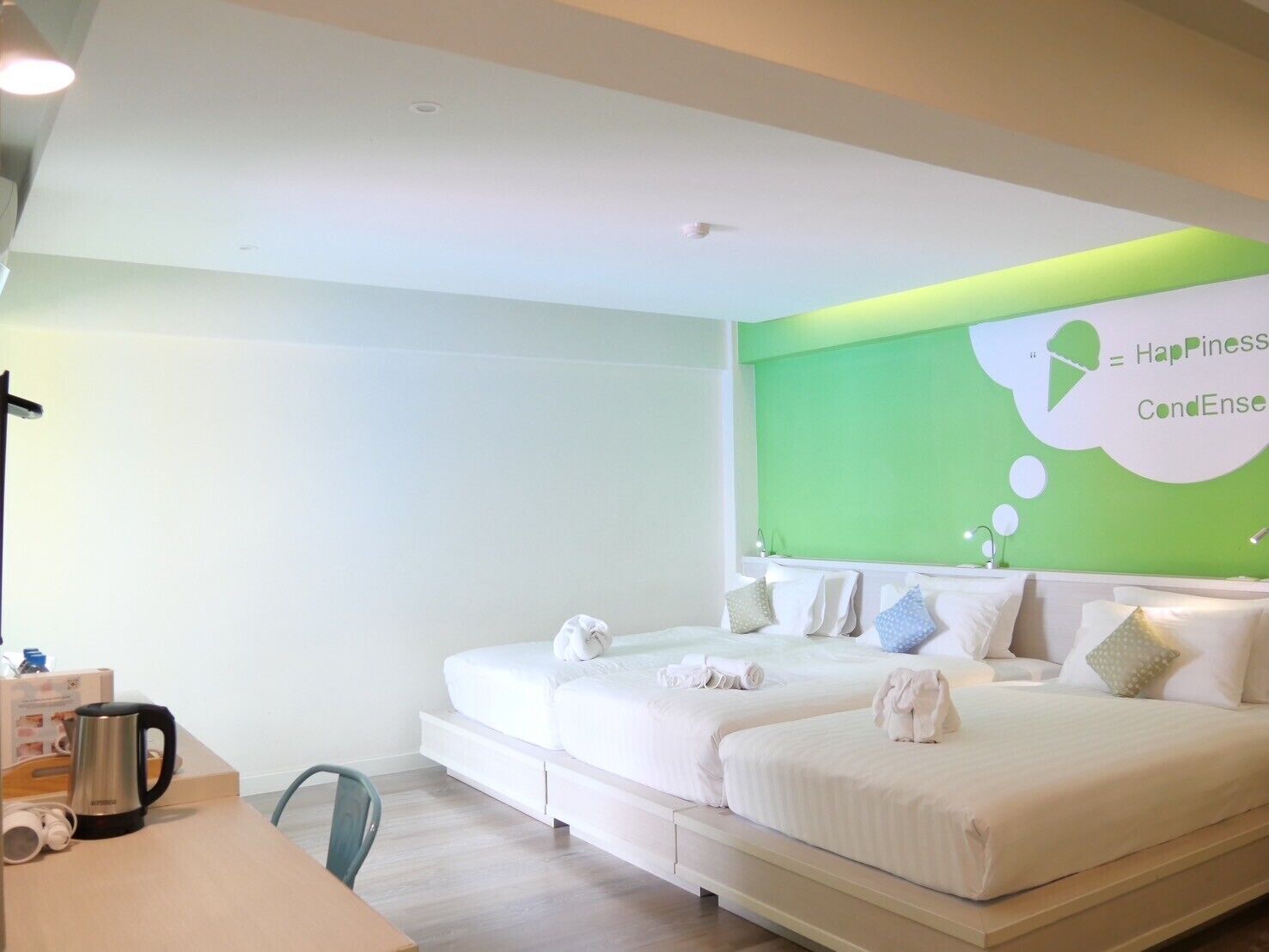 A modern hotel room with two beds, a desk, and a green accent wall.
