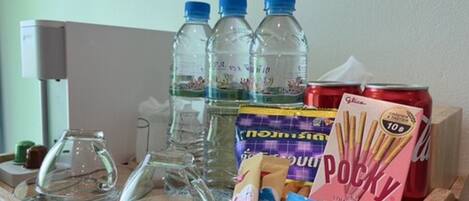 A table with a glass pitcher, three water bottles, a can of soda, a box of Pocky, and a bag of snacks.