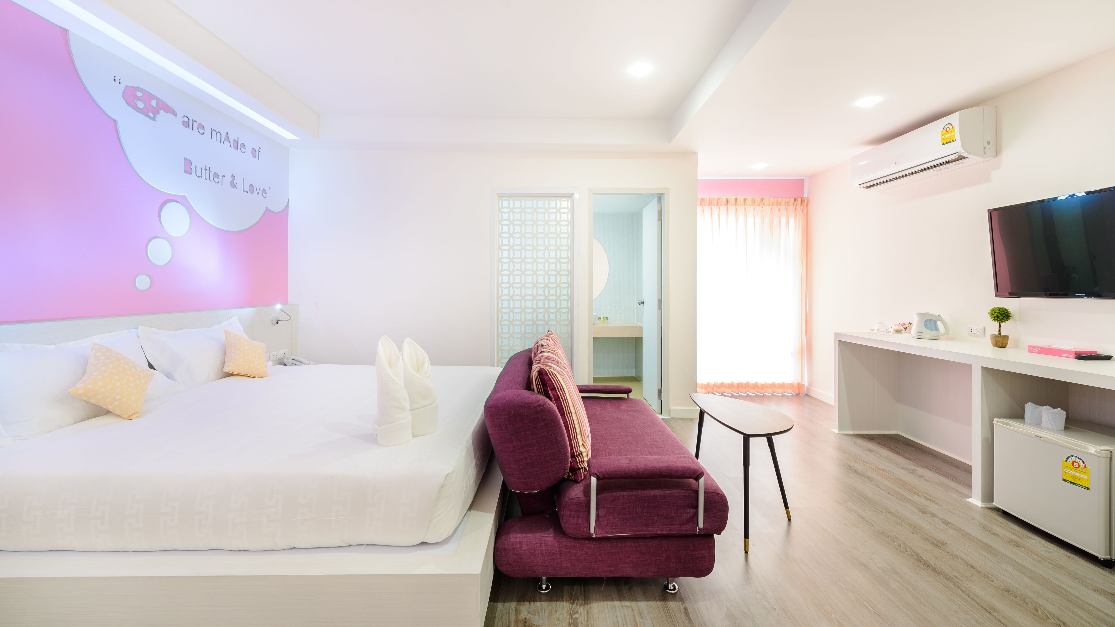 A modern hotel room with a bed, a sofa, a TV, and a desk.