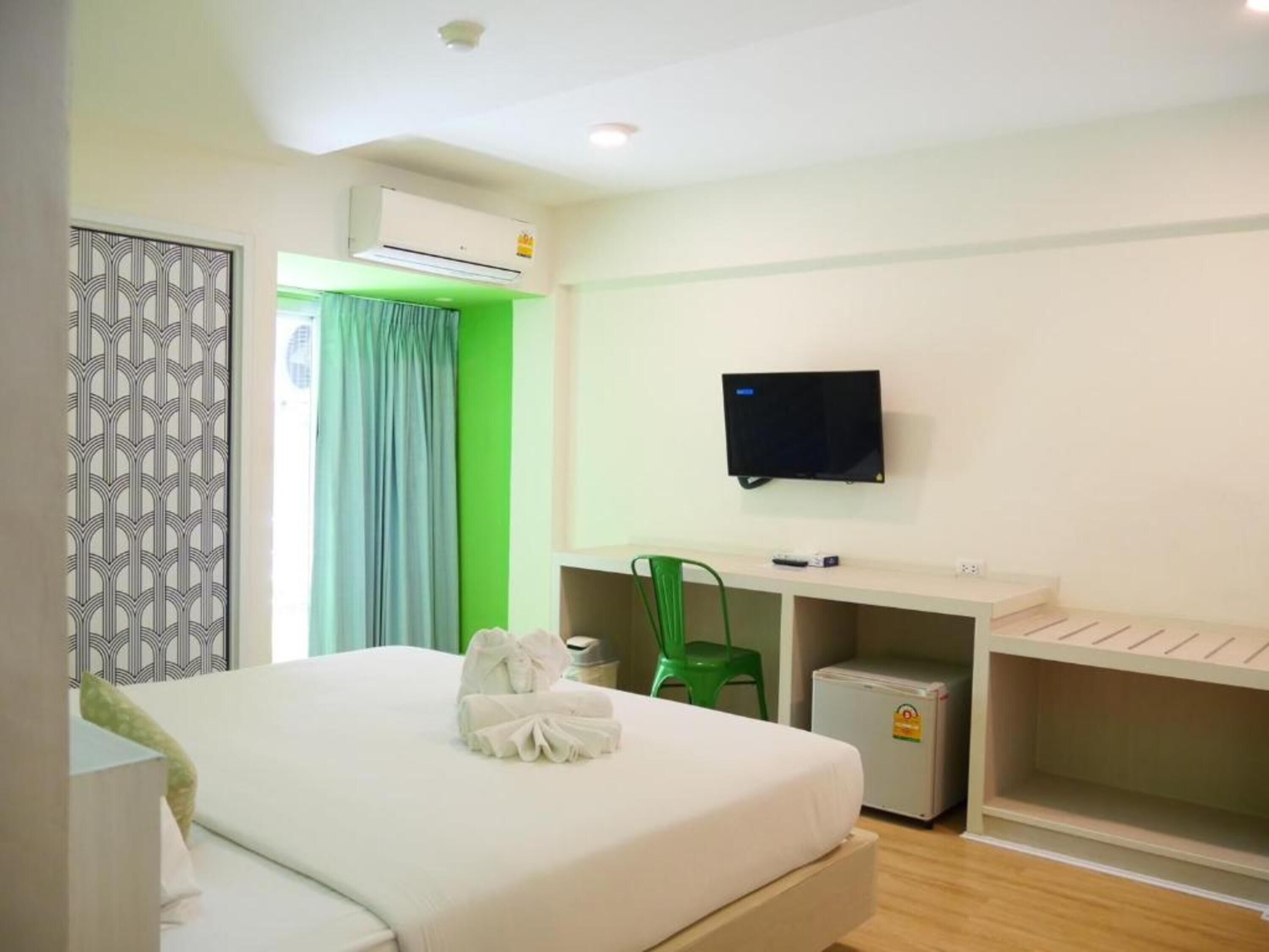 Ein Hotelzimmer mit Bett, Wandfernseher, kleinem Kühlschrank und Schreibtisch mit Stuhl.