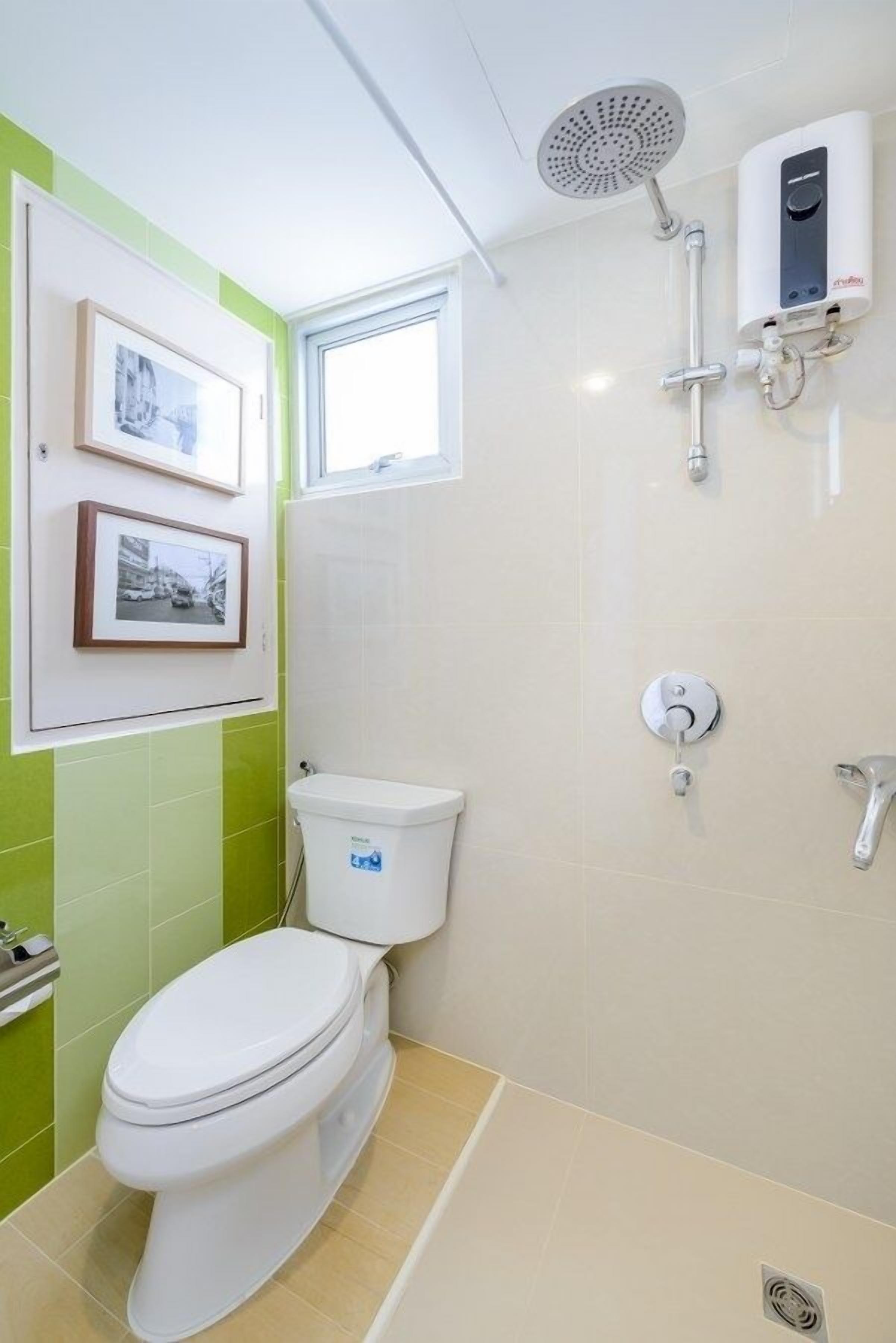 A bathroom with a toilet, a shower, and a wall-mounted heater. There are two framed pictures on the wall.
