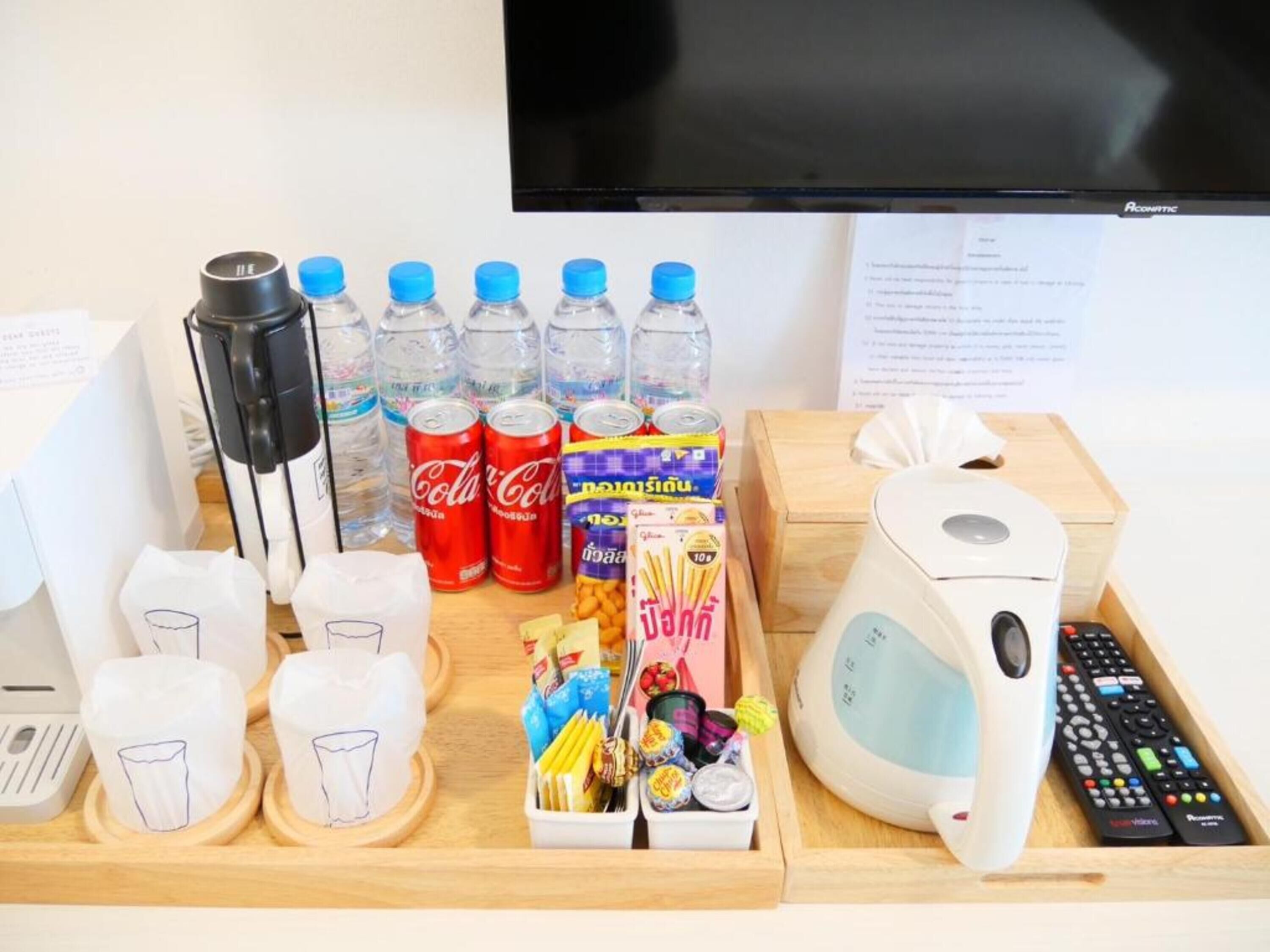 Una bandeja con botanas, agua embotellada y Coca-Cola, además de una tetera y controles remotos.