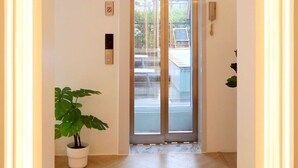 Pasillo que conduce a un ascensor, con una planta en maceta y un aplique de pared.