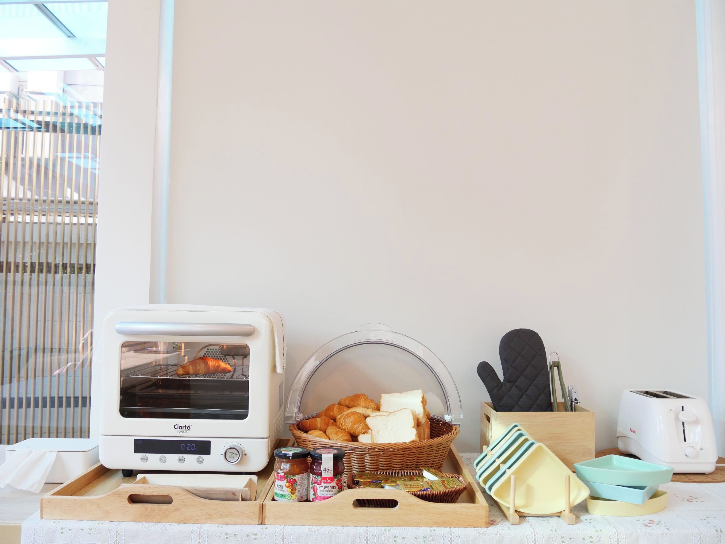 A kitchenette with a toaster, a bread basket, jars of jam, and a wooden tray.