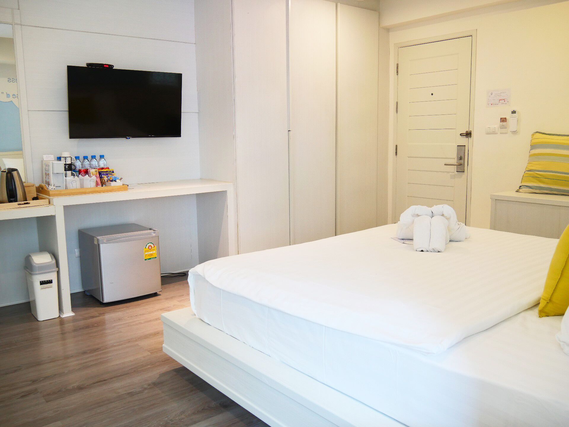 Ein Hotelzimmer mit Bett, Wandfernseher, Schreibtisch mit Kaffeemaschine und Mülleimer.