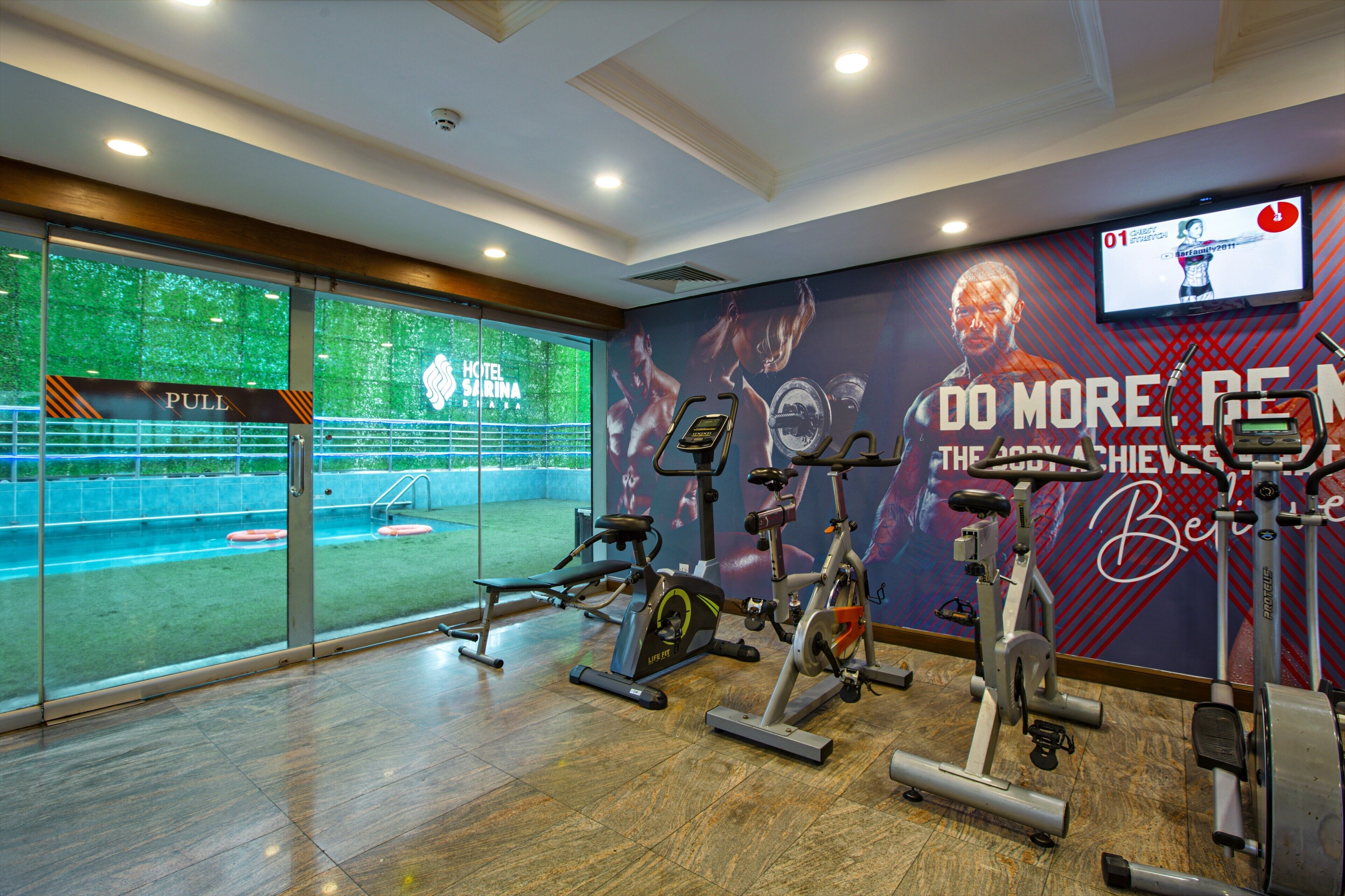 A gym with exercise equipment, a pull station, and a large window with a view of a pool.