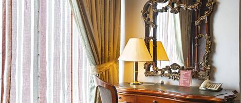A wooden desk with a lamp, a telephone, and a mirror with ornate detailing.