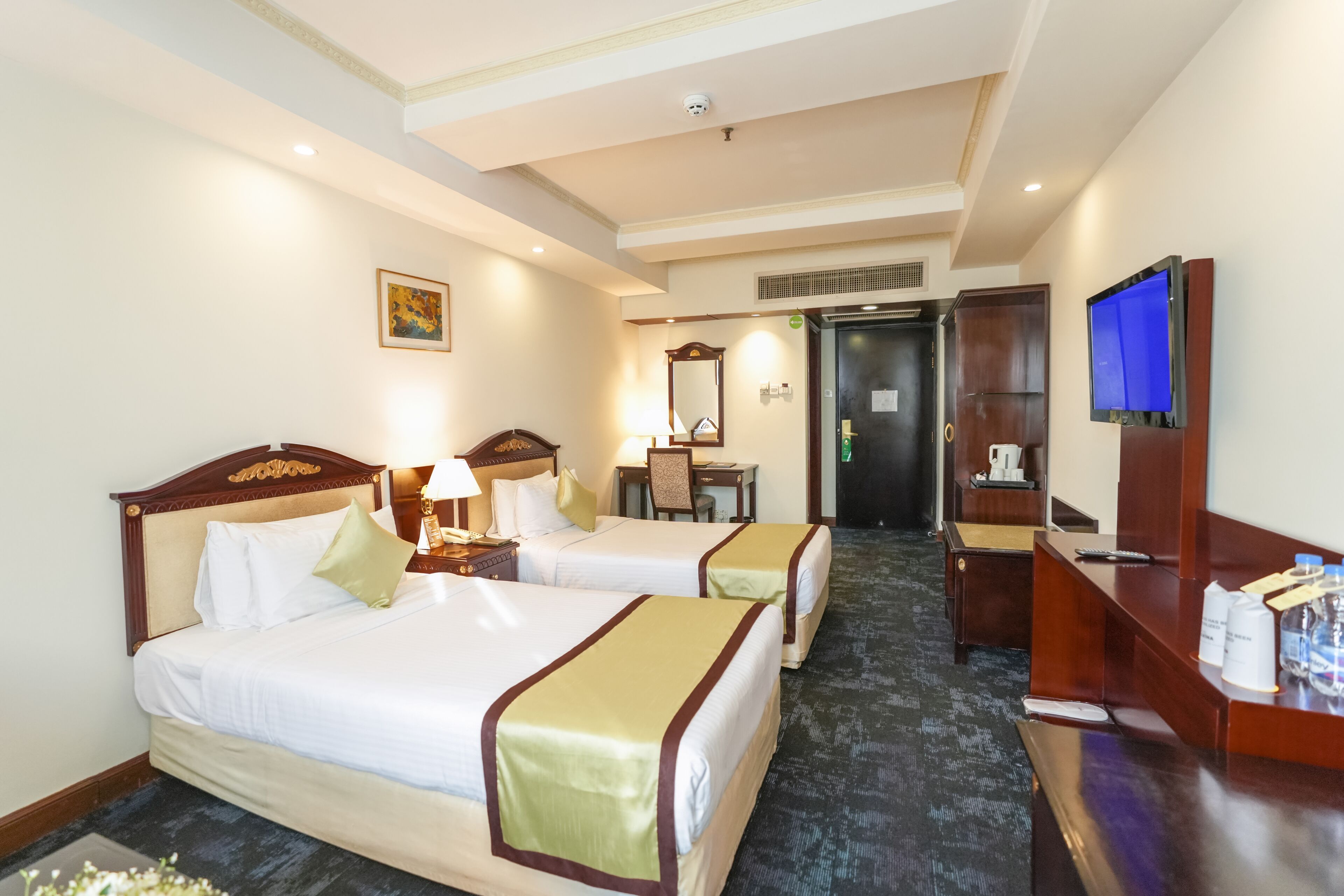 A hotel room with two beds, a desk, a television, and a reception area.