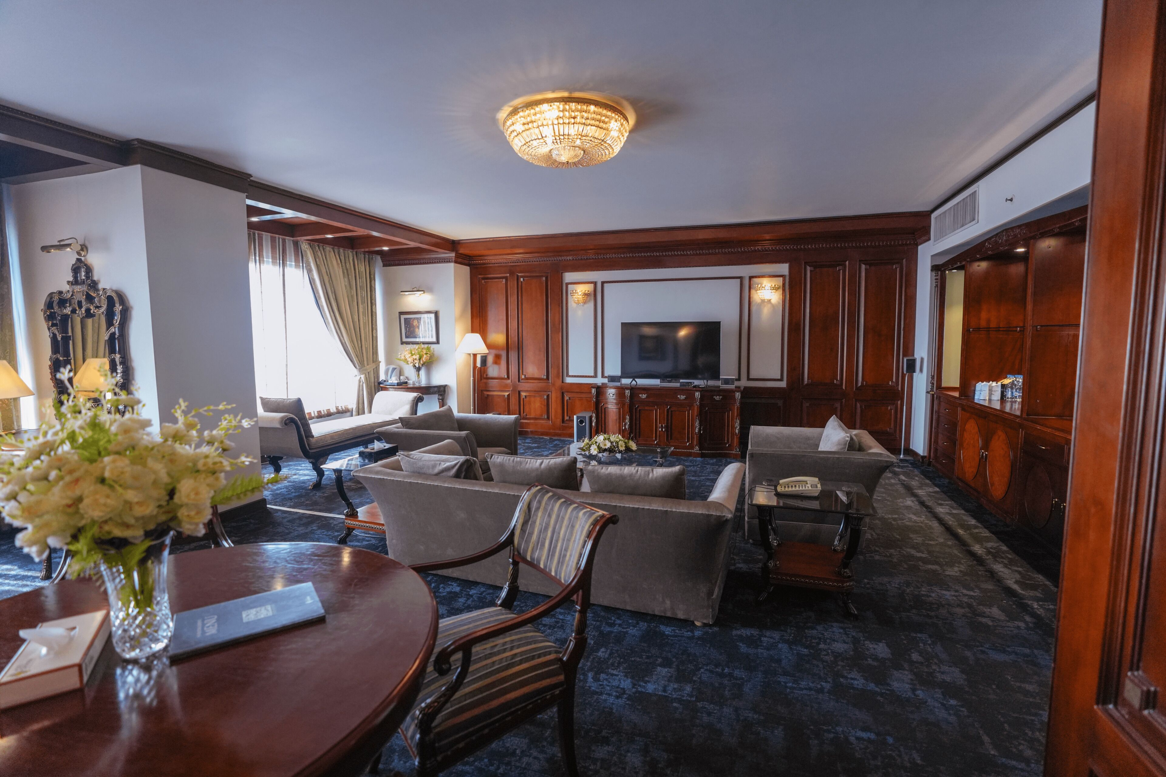 A hotel room with a living area featuring a sofa set, a television, and a chandelier.