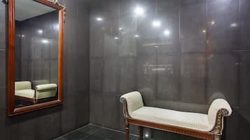 Bathroom features a large mirror, a bench, and a small plant, set against dark, glossy tiles.
