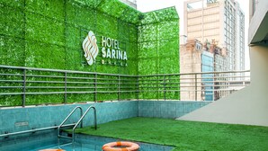 Una piscina interior con césped artificial, un flotador salvavidas y un cartel para el Hotel Sarina Dhaka.