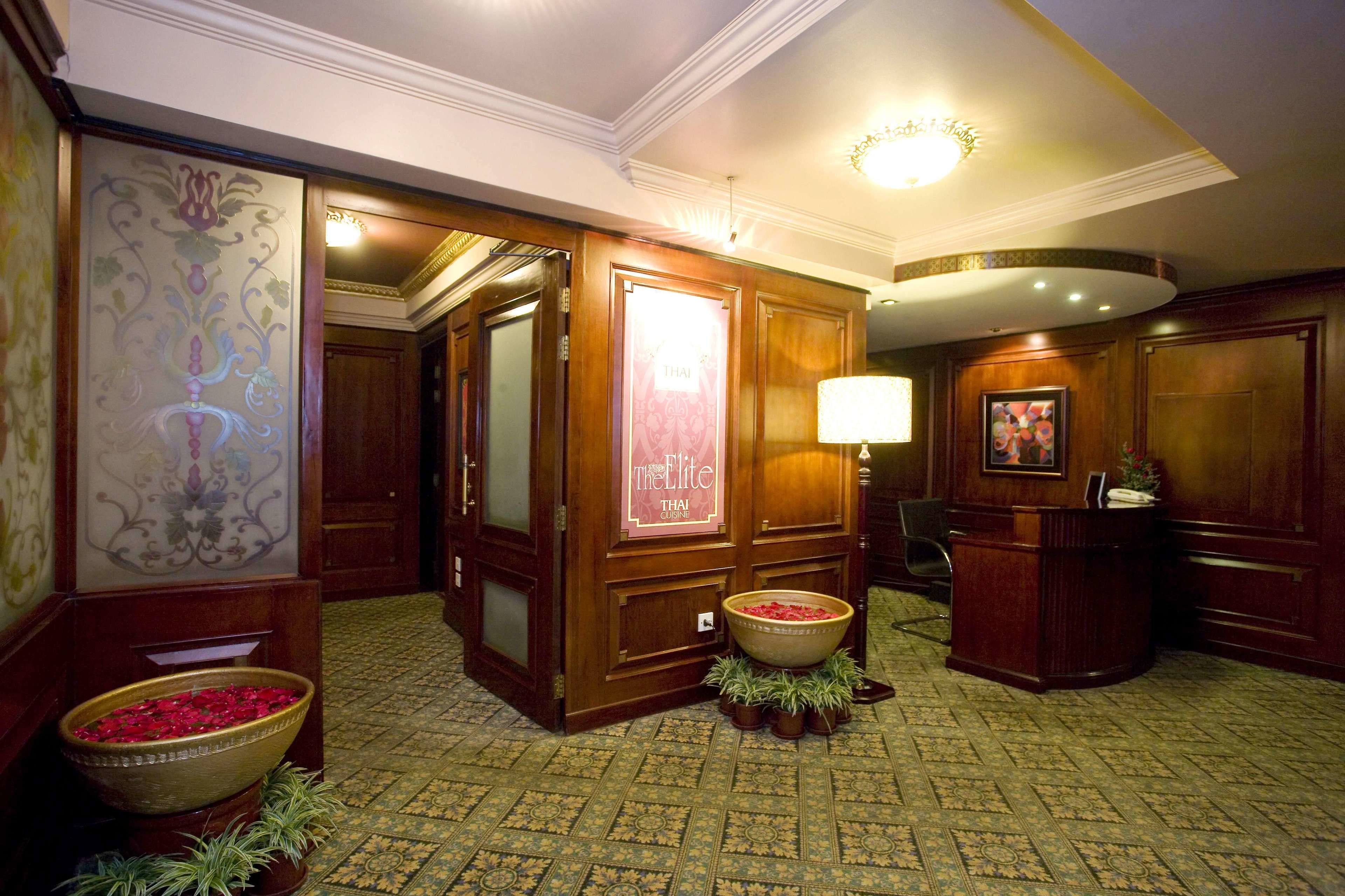 A lobby with a reception desk, a large decorative wall, a patterned carpet, and a floral arrangement.