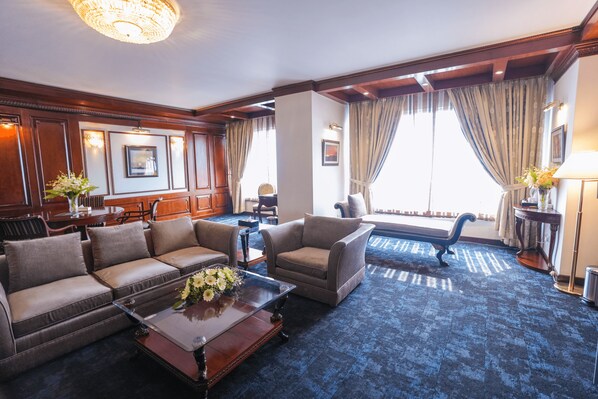 Amplia sala de estar con alfombra azul oscuro, sofás de cuero y una mesa de centro de madera con un jarrón de flores.