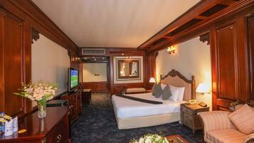 Habitación de hotel con una cama grande, televisor, escritorio con un florero, una silla y una mesita de noche con lámpara.